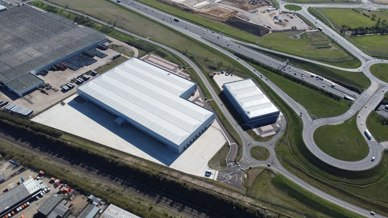 Aerial view of two logistics buildings edged by hedgerows and a brook